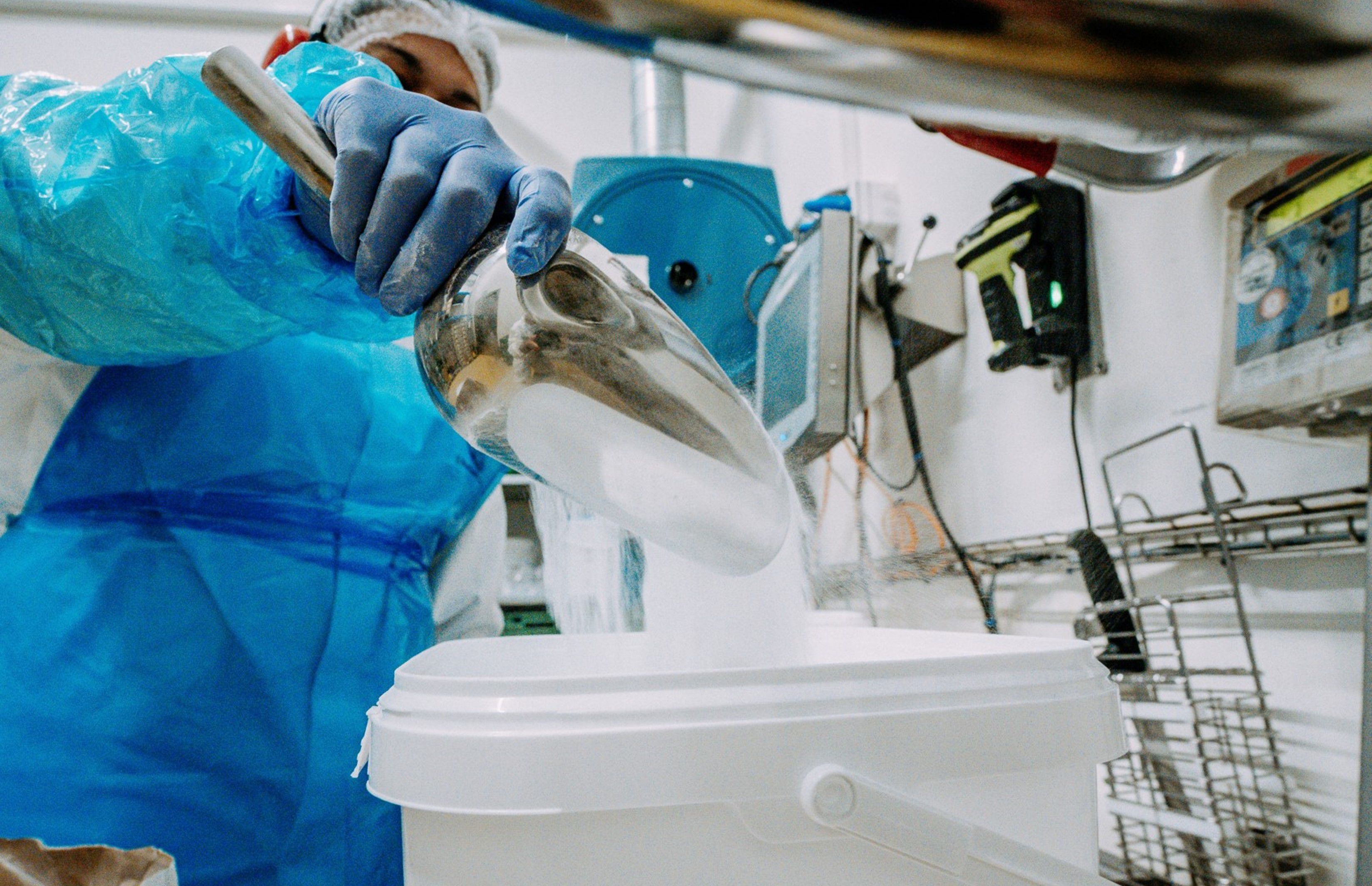 Une employée de Bigler remplit des épices dans des seaux en plastique blancs ; le bras d'aspiration Nederman NEX D est visible en haut.