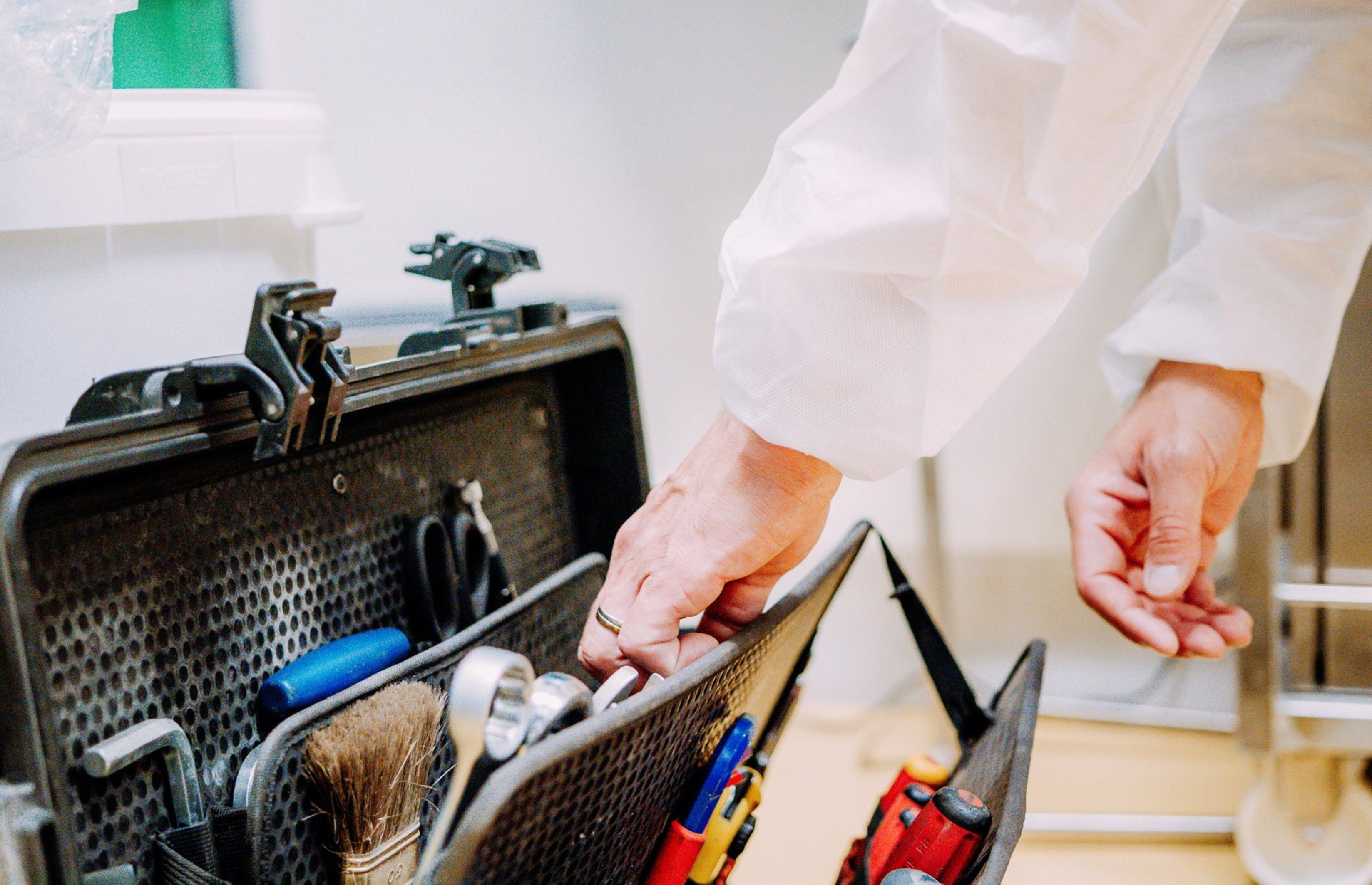 Des mains et des avant-bras plongent dans une boîte à outils ; une clé Allen, une clé à molette et un pinceau sont visibles.