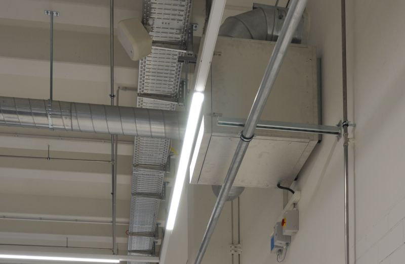 Deckeninstallation in einer Werkstatt mit Lüftungskanälen, Kabeltrassen, Leuchten und weiteren technischen Bauteilen.