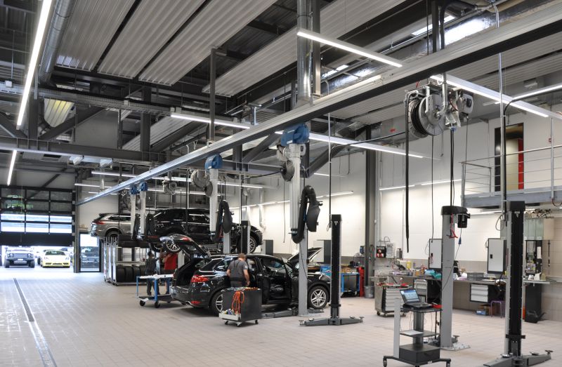 Innenansicht der Werkstatt der Porsche-Filiale in Bern mit mehreren Fahrzeugen auf Hebebühnen, Arbeitsplätzen und technischen Deckeninstallationen.