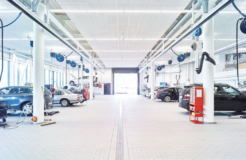 Große, moderne Kfz-Werkstatt mit vielen Hebebühnen und zahlreichen blauen Nederman Schlauchaufrollern an der Decke