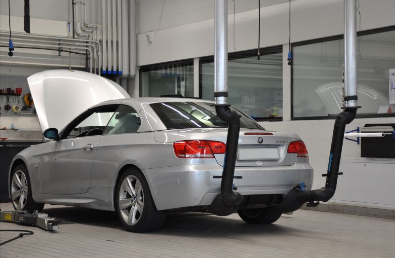 Silberner BMW in Werkstatt mit offener Motorhaube, angeschlossen an zwei Nederman Doppelabsaugstutzen