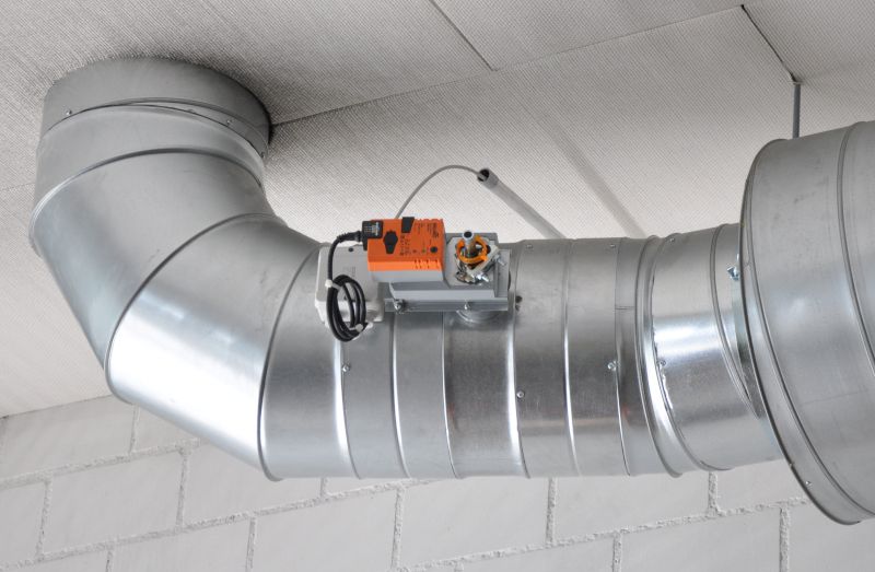 Conduit de ventilation rond avec un servomoteur électrique orange pour un clapet de régulation.