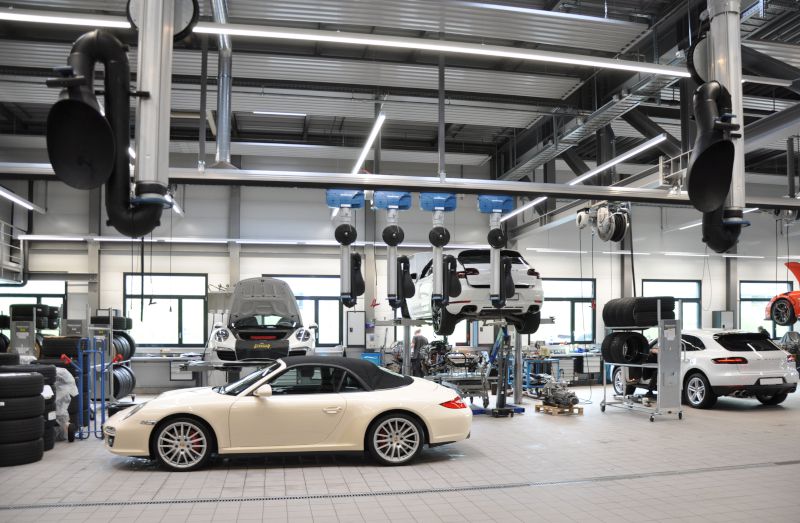 Innenansicht der Werkstatt der Porsche-Filiale in Bern mit mehreren Fahrzeugen auf Hebebühnen, Arbeitsplätzen sowie Schlauchaufrollern und Beleuchtung an der Decke.