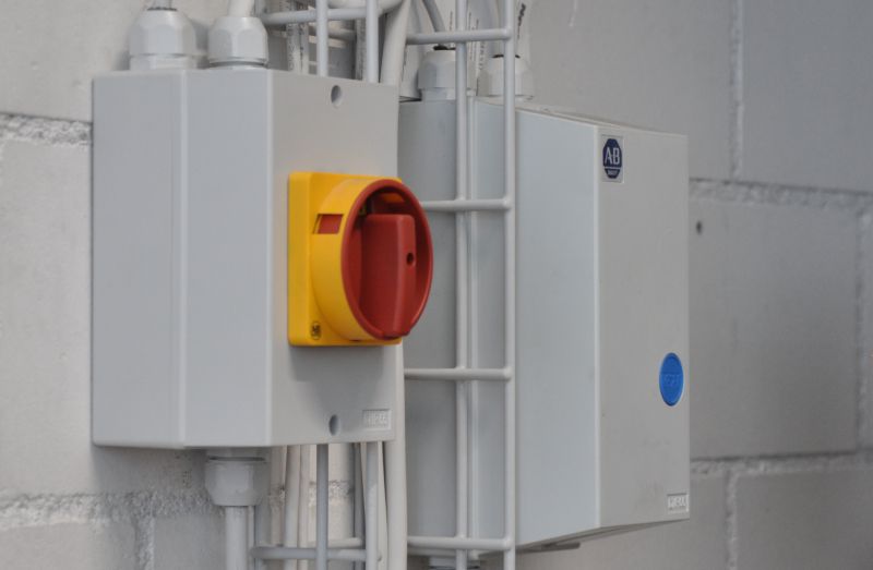 Interrupteur électrique principal jaune et rouge (sectionneur) à côté d'un boîtier électrique gris sur un mur en briques.
