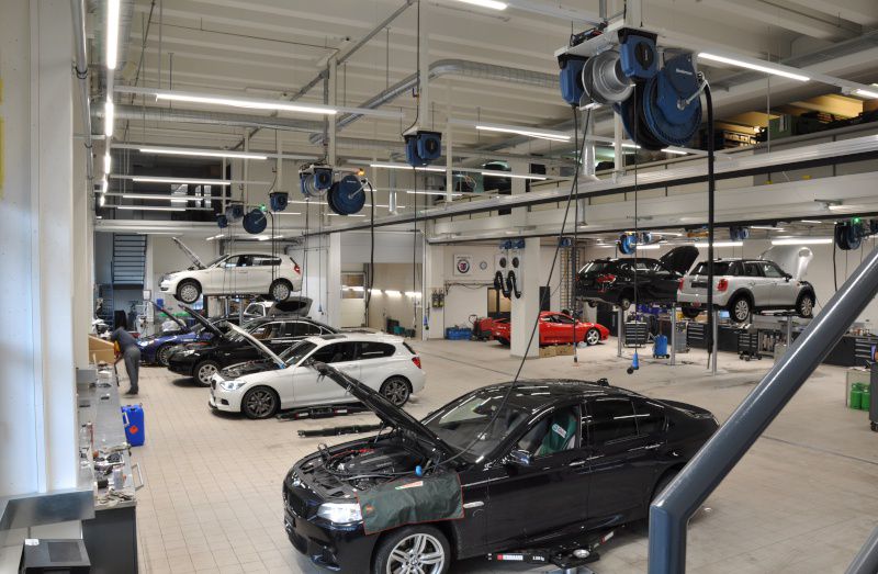 Autowerkstatt mit mehreren Autos, Autos auf Hebebühnen und Schlauchaufroller von Nederman an der Decke.