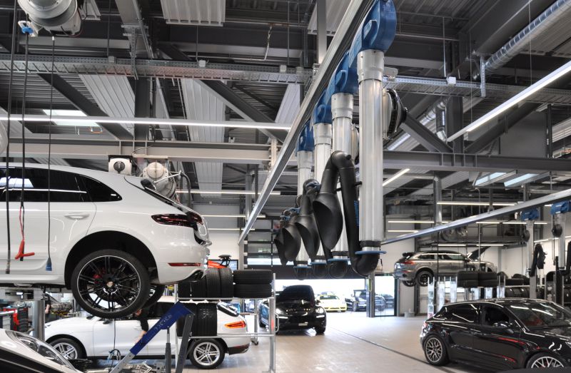 Innenansicht der Werkstatt der Porsche-Filiale in Bern mit Fahrzeugen auf Hebebühnen sowie deckenmontierten Absaugarmen und Beleuchtung.