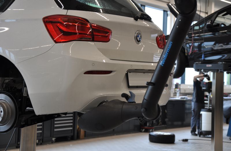 Hinteransicht eines weißen BMW auf Hebebühne, angeschlossen an Nederman Abgasabsaugarm mit Trichter.