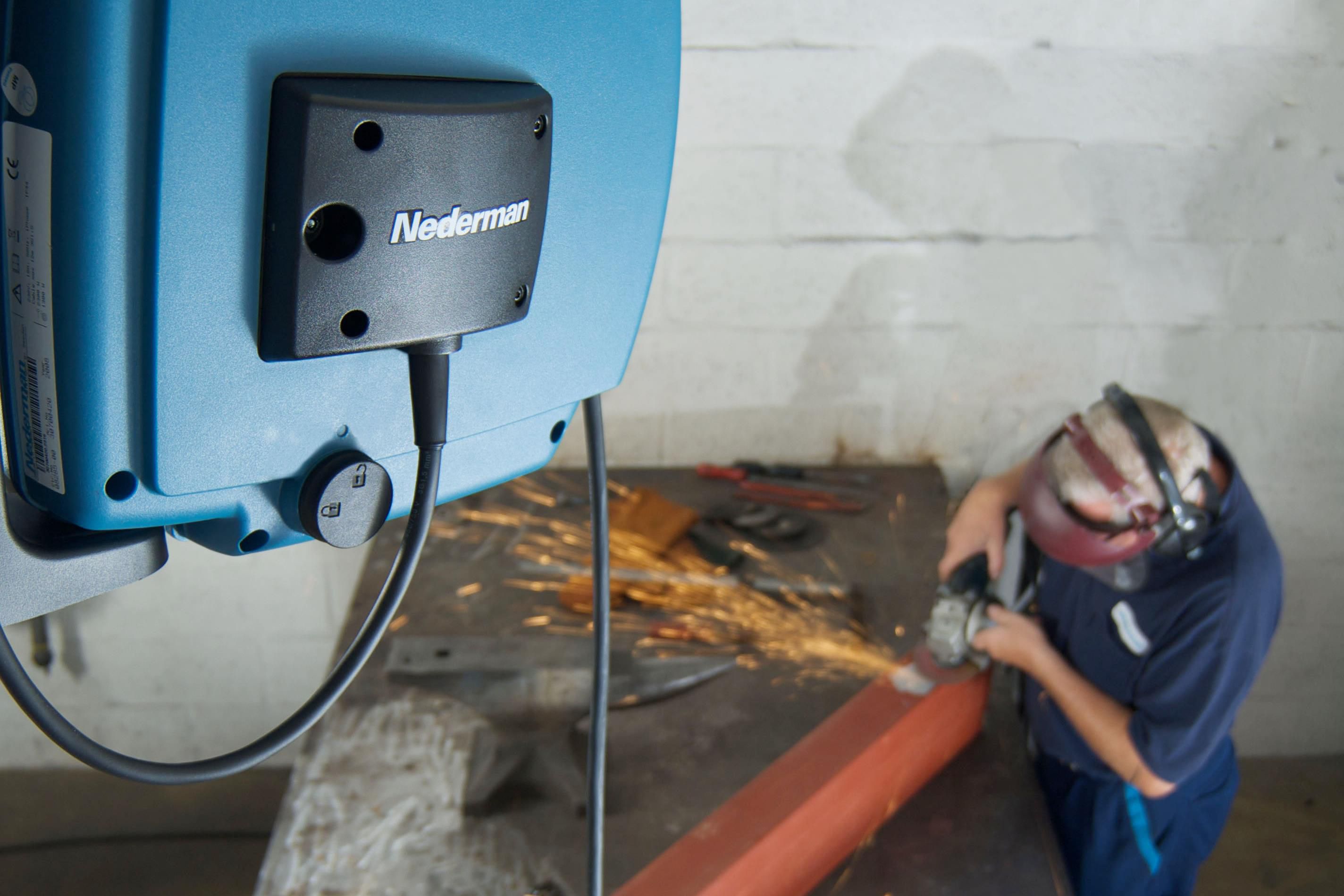Enrouleur de câble Nederman C20 monté sur le mur de l'atelier, avec une personne effectuant des travaux de soudage en dessous.