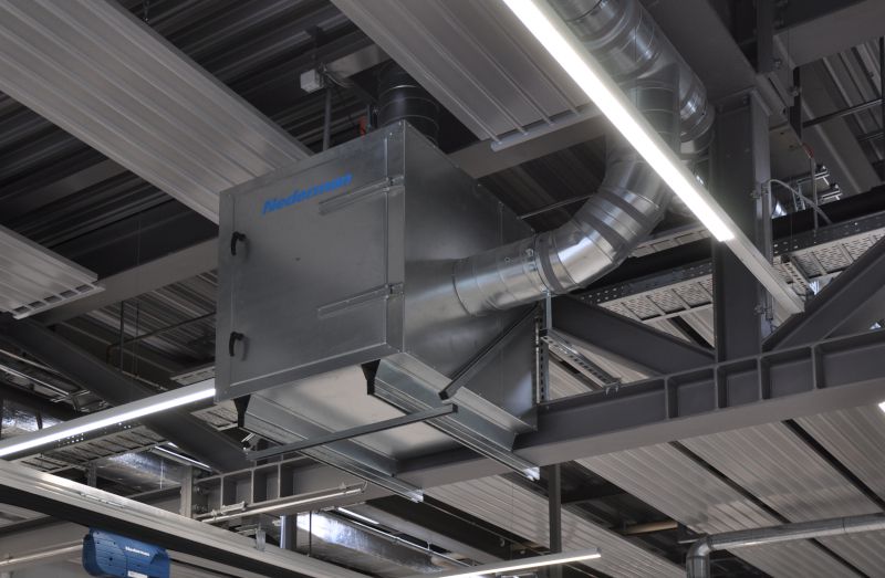An der Decke montierte Nederman-Absaugeinheit in einer Werkstatt mit metallischen Rohrleitungen und sichtbarer Beleuchtung.
